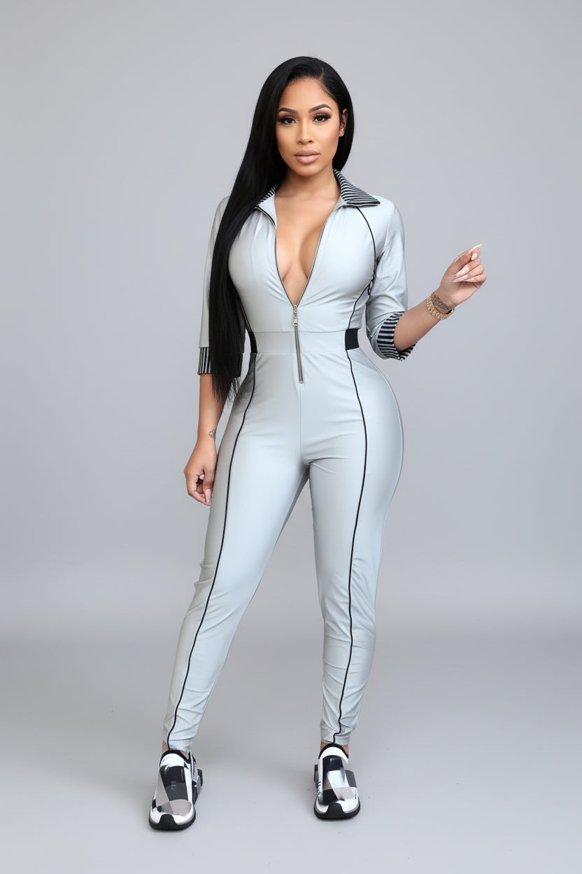 A woman wearing a light gray jumpsuit with black accents is standing against a modern building exterior.