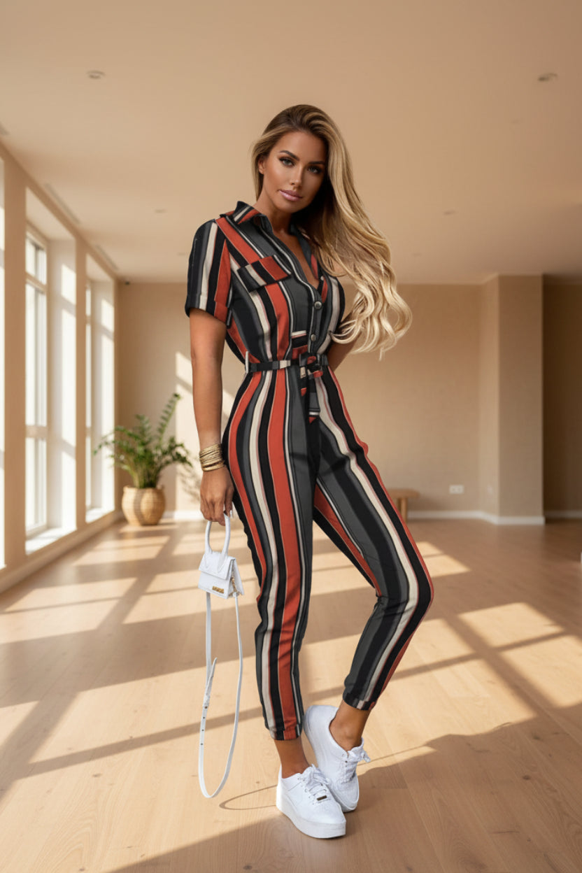 A woman wearing a striped jumpsuit is standing against a beige wall.