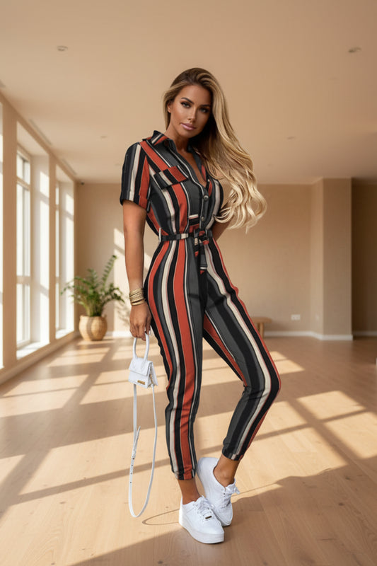 A woman wearing a striped jumpsuit is standing against a beige wall.