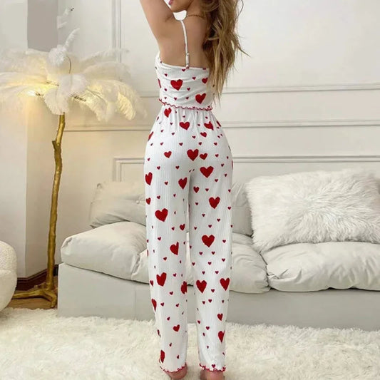 A woman wearing a white pajama set with red heart patterns in a bedroom.