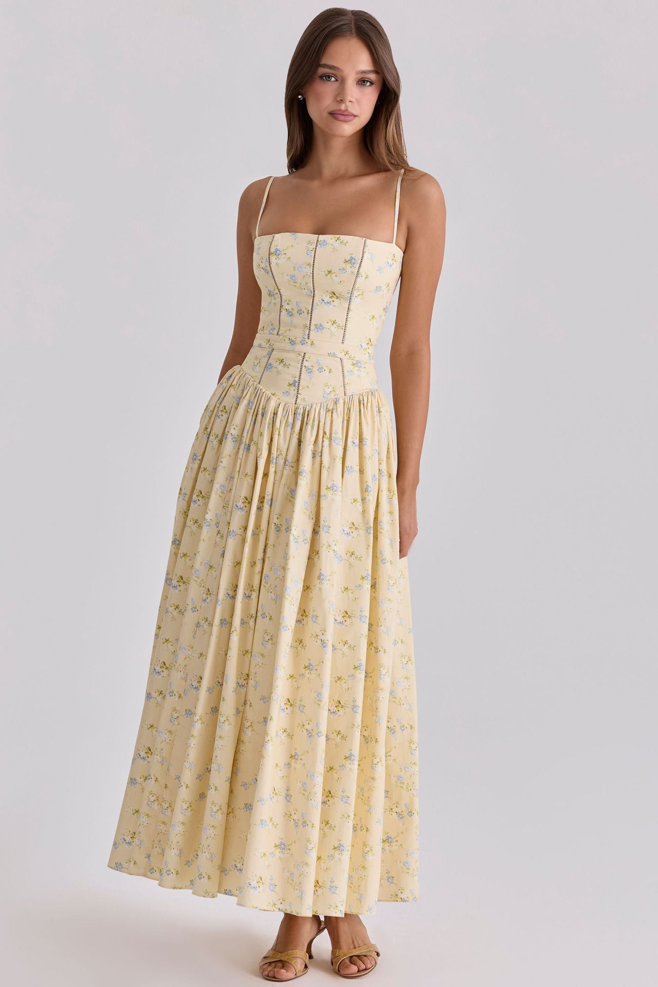 Woman wearing a yellow floral dress against a plain background