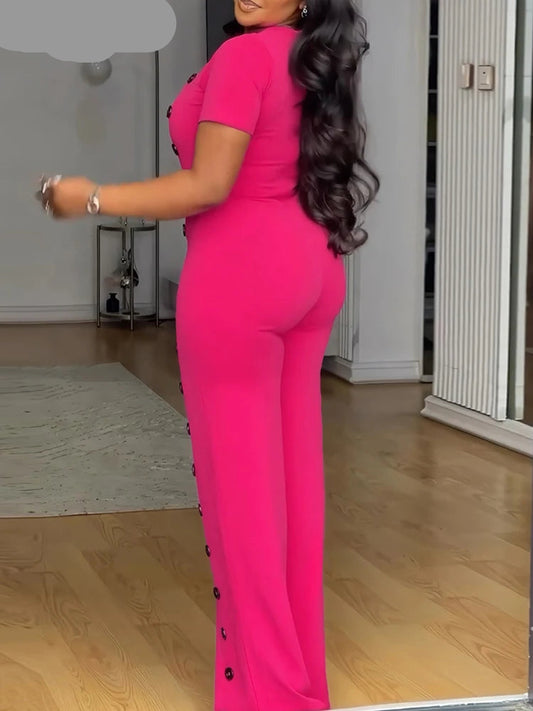 Person wearing a bright pink jumpsuit with black buttons in an indoor setting.