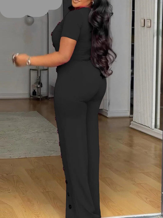 Woman wearing a black jumpsuit in a room with wooden flooring.