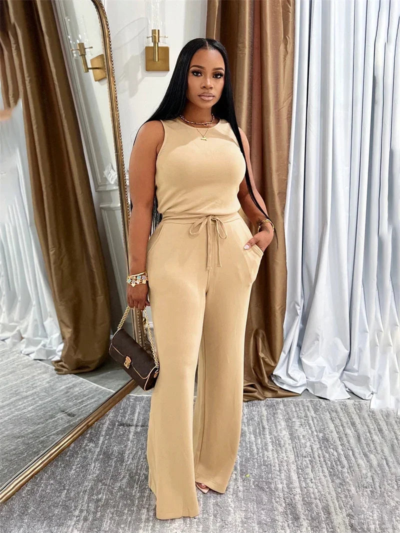 Woman in a beige jumpsuit standing in front of a mirror with curtains in the background