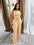 Woman in a beige jumpsuit standing in front of a mirror with curtains in the background